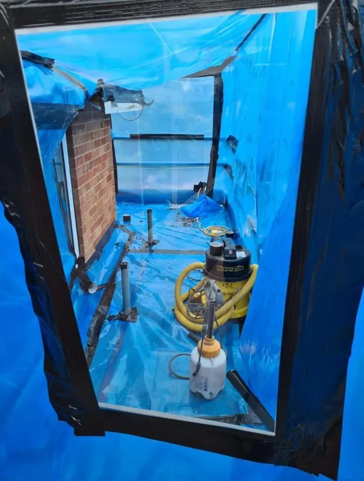 A controlled asbestos removal enclosure with blue protective sheeting and industrial vacuum equipment.
